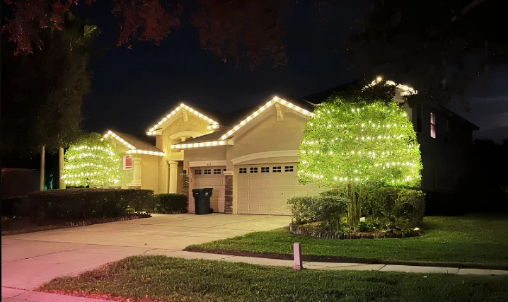 Home with warm white roofline lighting and glowing Christmas trees