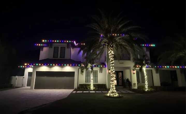 White modern home with a palm tree wrapped in colorful Christmas lights