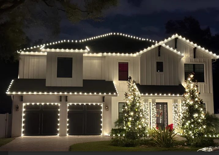Modern white farmhouse with warm white roofline and tree lighting