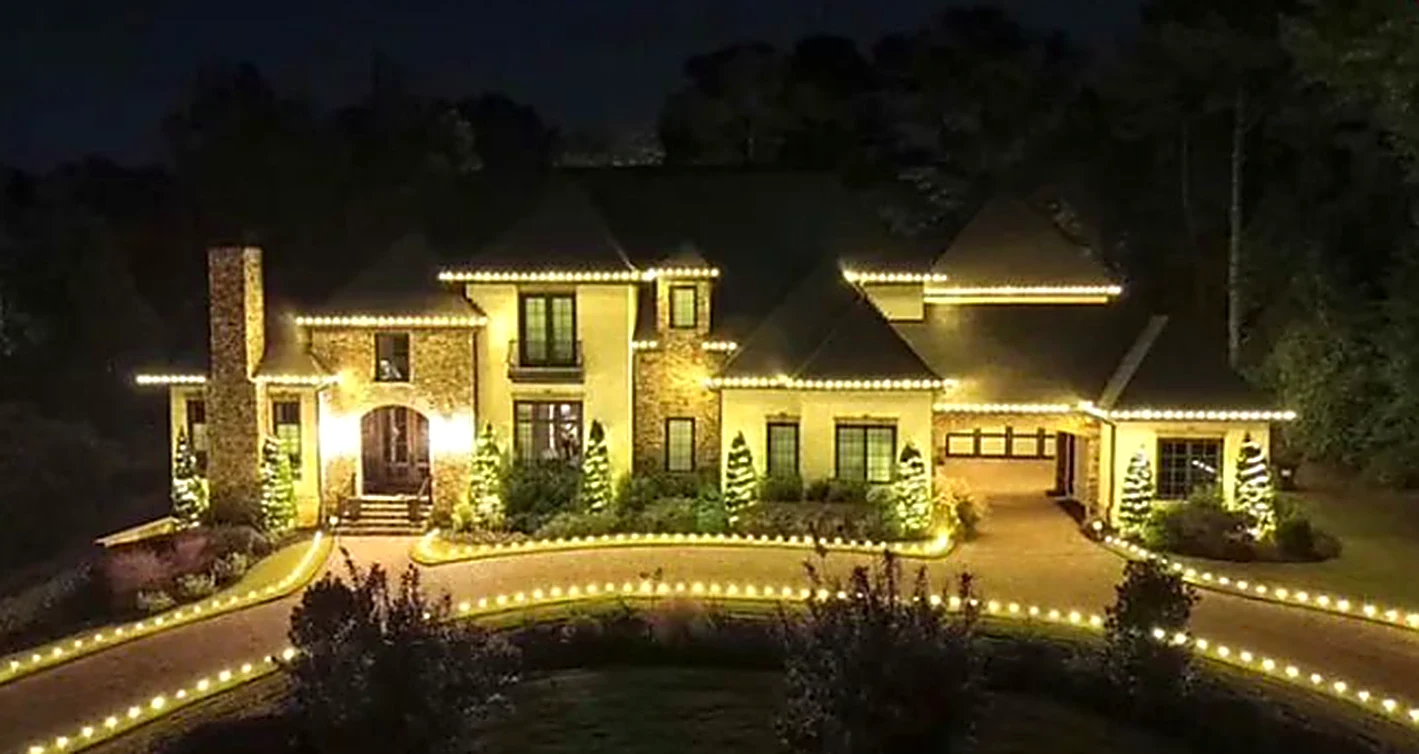Large two-story stone and stucco estate home with warm white roofline lighting and a lit circular driveway