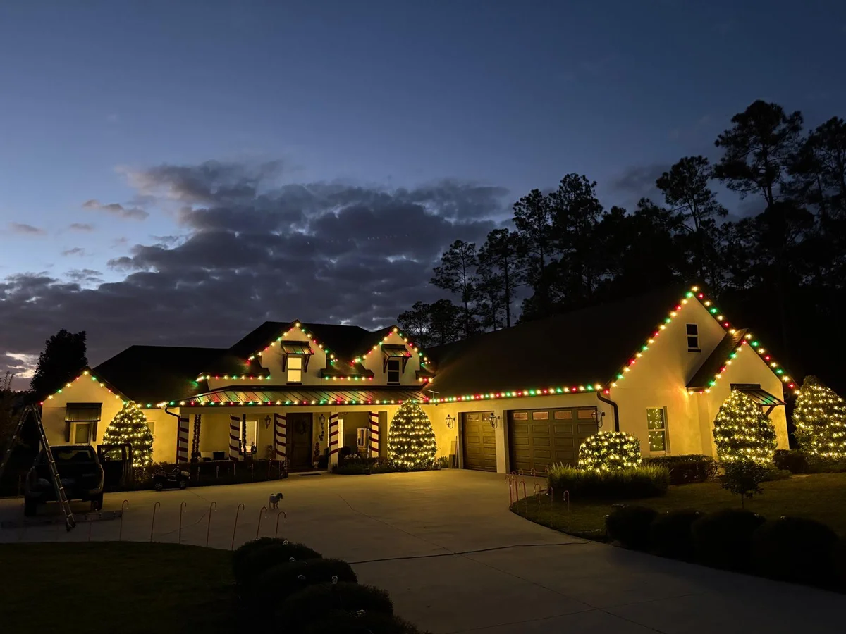 Florida estate home with red and green roofline and dormer lighting and lit shrubs