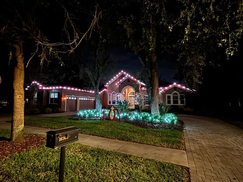 Home in FishHawk, FL with red and white roofline Christmas lighting and a lit JOY yard display