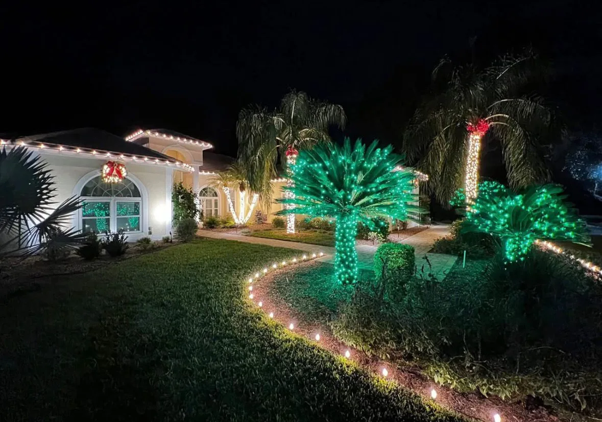 Estate home in Tampa, FL with palm trees wrapped in green Christmas lights and a lit wreath